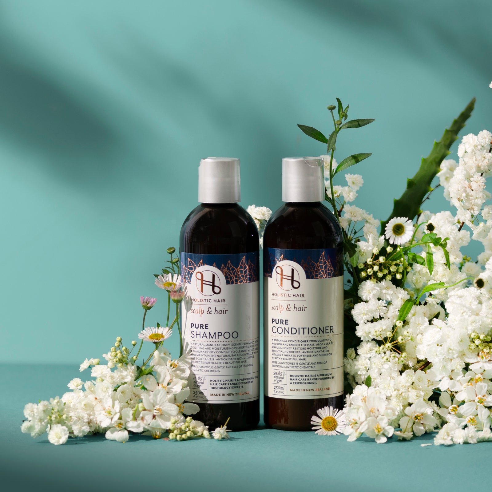Two bottles of Pure shampoo and conditioner with flowers on a teal background