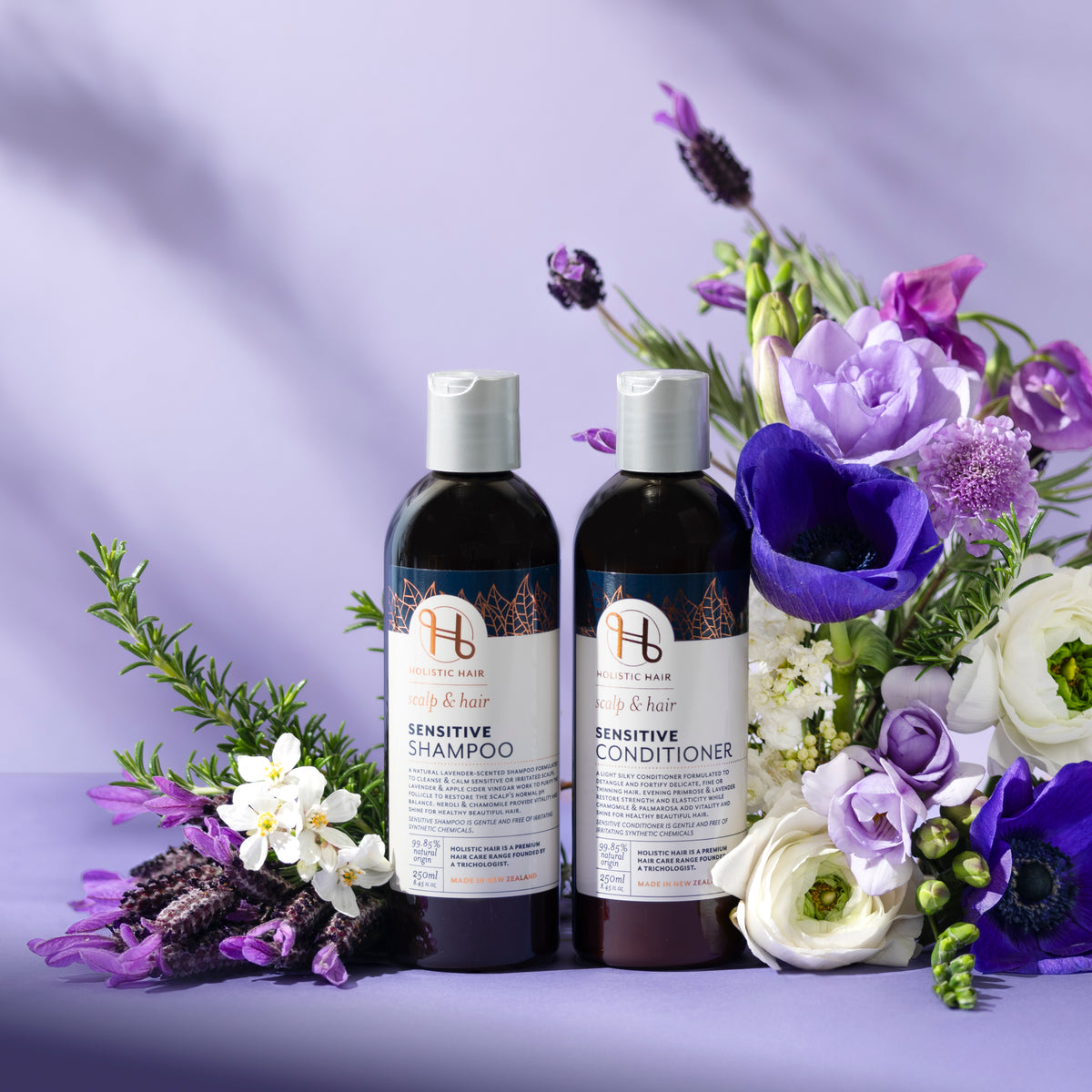 Two bottles of sensitive shampoo and conditioner with flowers on a purple background.