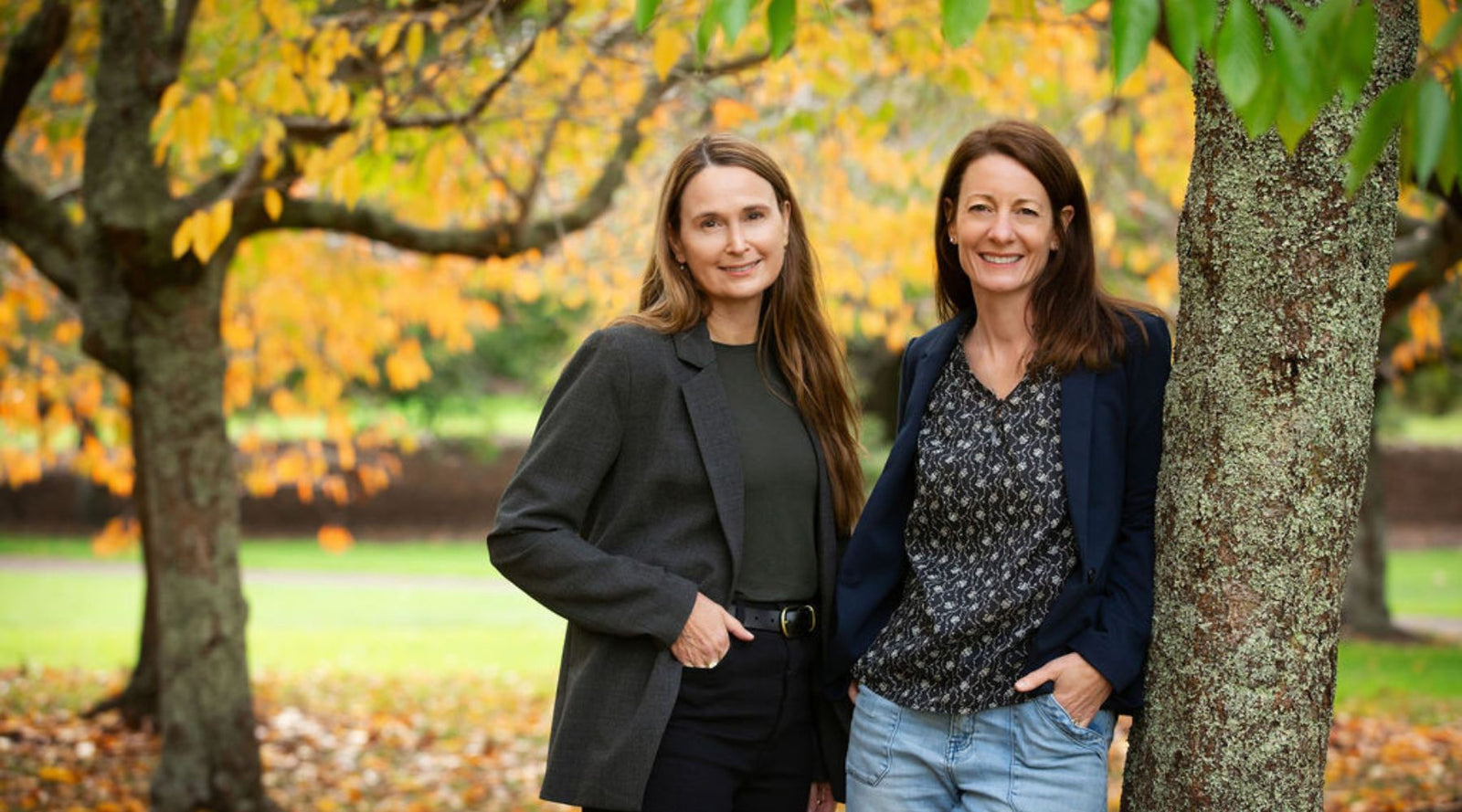 Nicky & Jodene, co-owners of Holistic Hair, standing with a nature background.